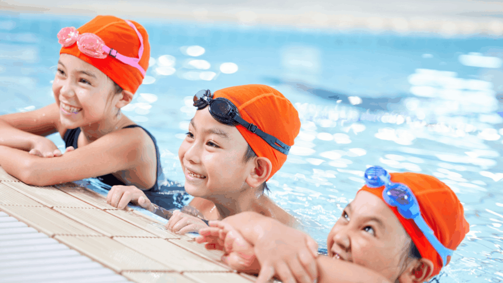 Kids in swim caps and goggles enjoying swimming lesson